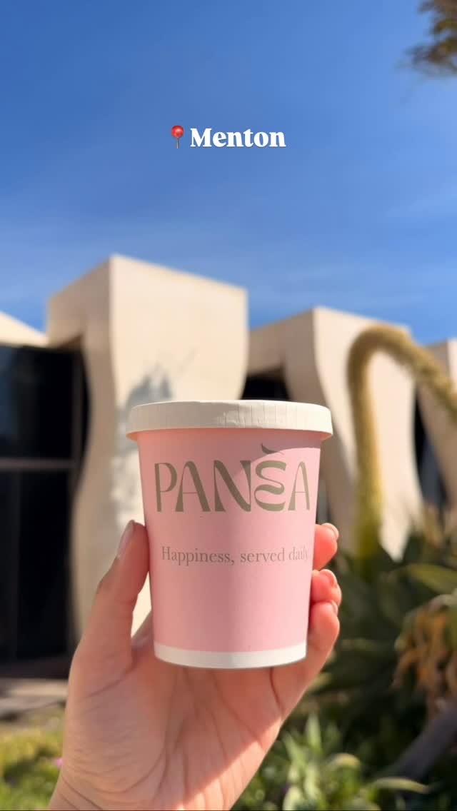 Un gobelet PANÈA « Happiness, served daily » tenu devant l'architecture de Menton